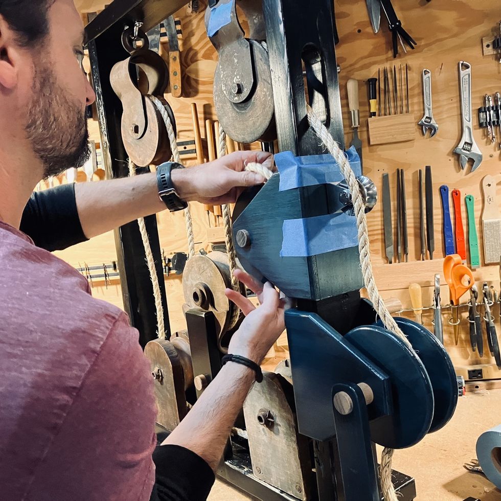 Person adjusting a blue pulley system in a workshop with tools on the wall.
