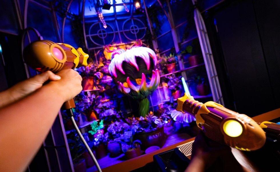 Person aiming toy lasers at a giant, colorful animatronic plant in an arcade setting.