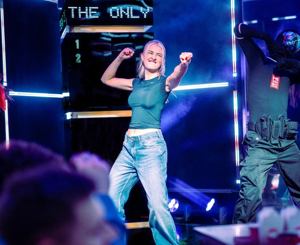 Person dancing energetically on a colorful stage with vibrant lights and effects.