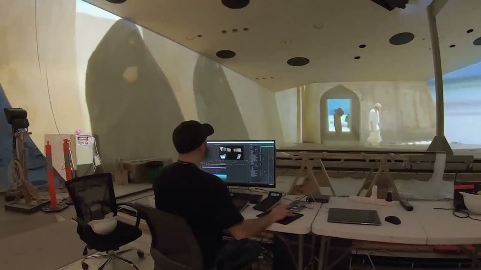 Person editing video for National Museum of Qatar with large projected images on a curved wall.