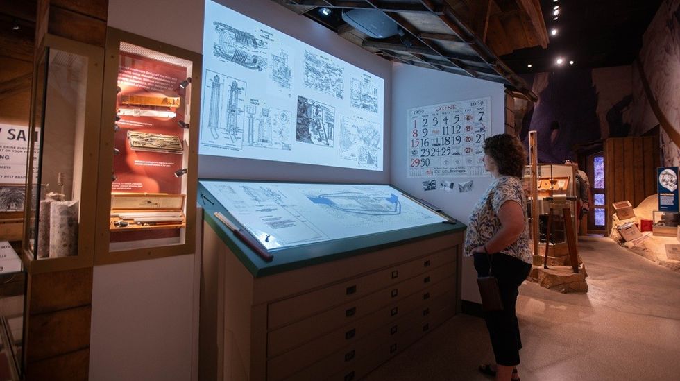 Person examines historical exhibits and diagrams in a dimly lit museum display.