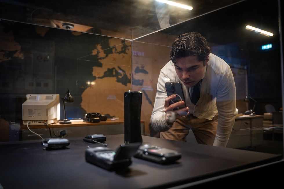 Person examines old mobile phones in museum exhibit, The Mind of a Serial Killer: The Experience.