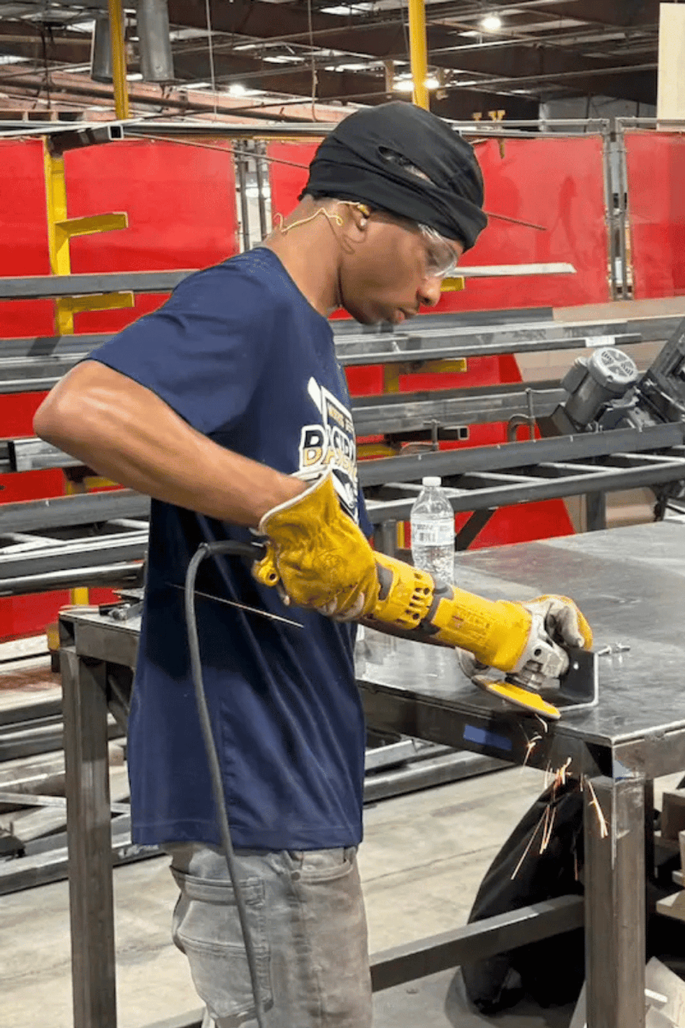 Person grinding metal with a power tool in a workshop, wearing safety gear.