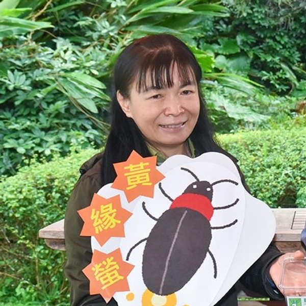 Person holding a large drawing of a bug with colorful text, standing outdoors.
