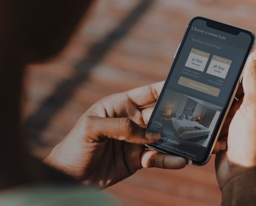 Person holding a phone displaying a hotel booking app with room options.