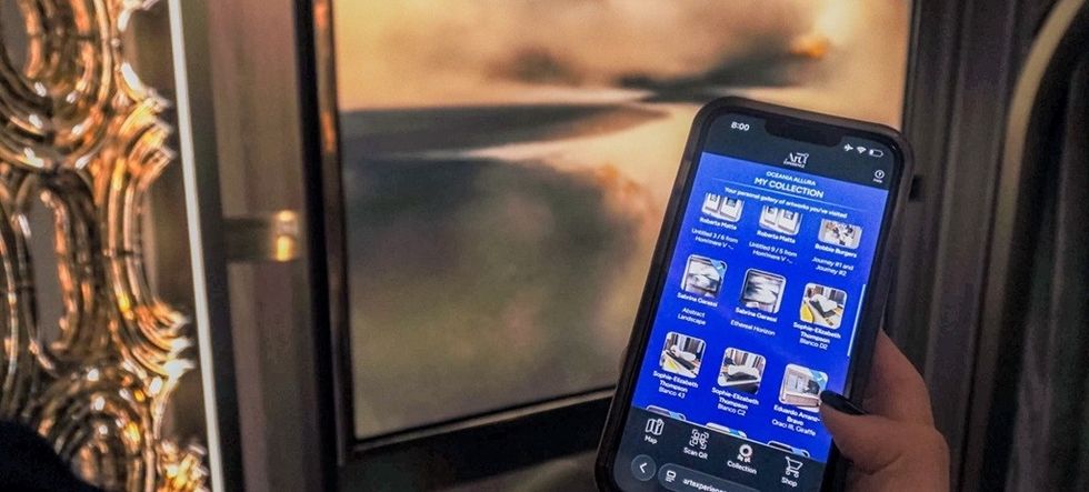 Person holding a phone with a blue app screen in front of a large wall display.