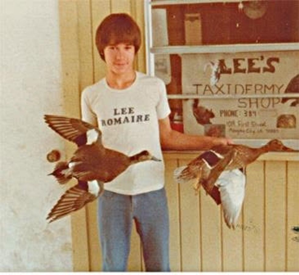 Person holding mounted ducks in front of Lee's Taxidermy Shop.
