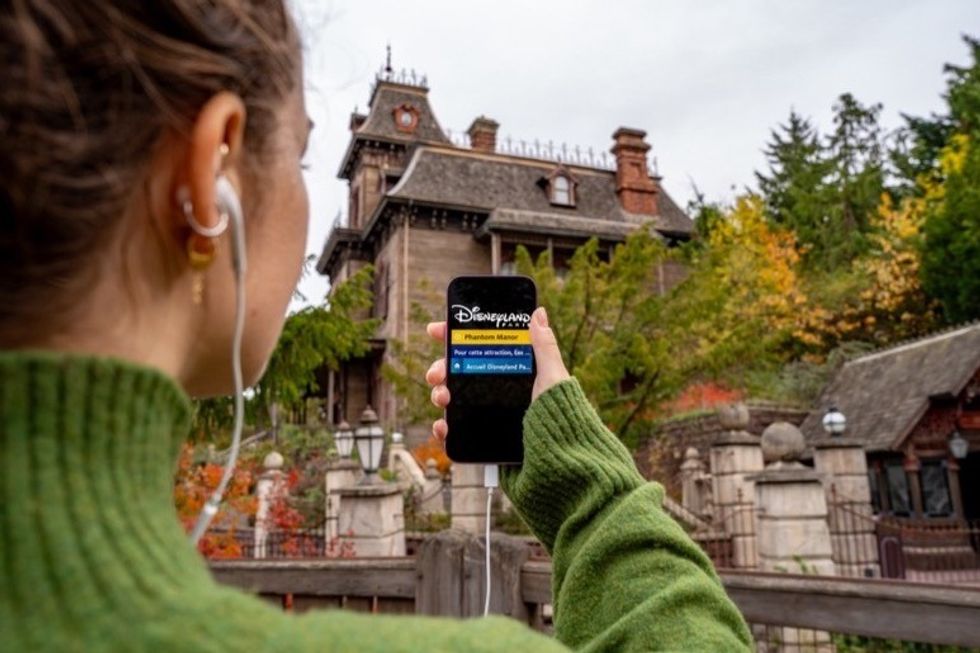 Person holding smartphone with Disneyland audio description app in front of a haunted mansion.