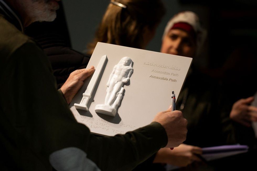 Person holding tactile 3D map with Braille, featuring an obelisk and a standing figure.