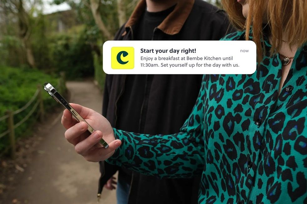 Person holds a phone showing a breakfast notification in a park setting.