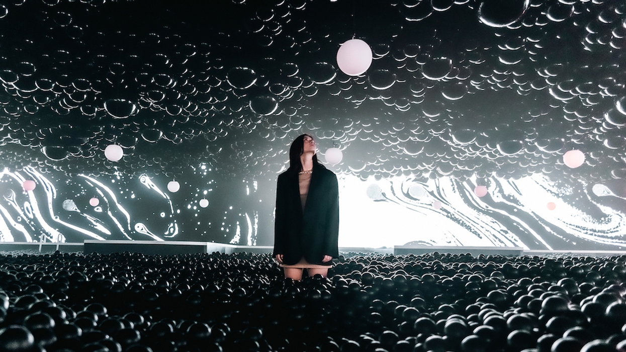 Person in a dark room with a swirling light pattern, surrounded by black balls and hanging spheres.