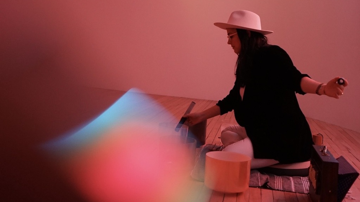 Person in a hat playing crystal singing bowls, surrounded by soft red lighting.