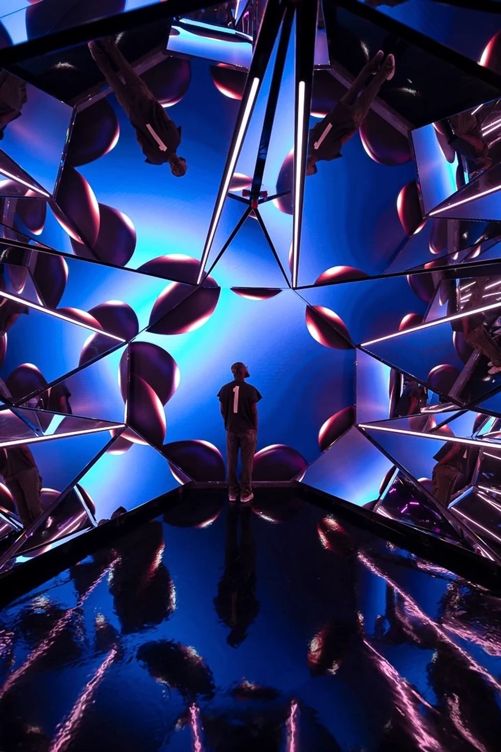 Person in a mirrored room with blue and purple futuristic lights and reflections.