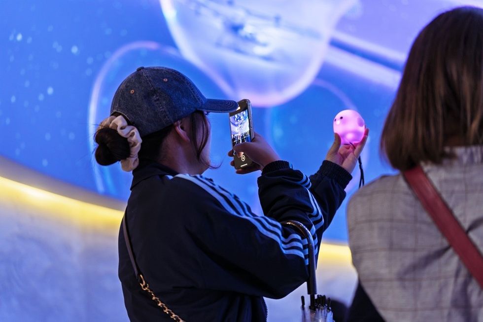 Person in cap takes a photo of a glowing object with their phone against a starry background.