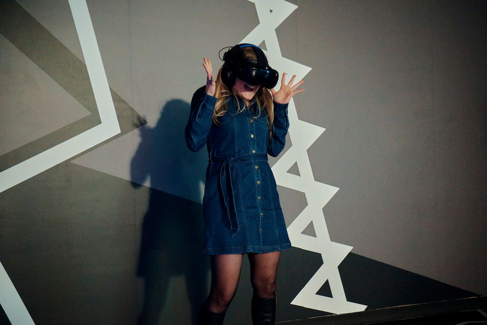Person in denim dress, excitedly using VR headset against geometric background.