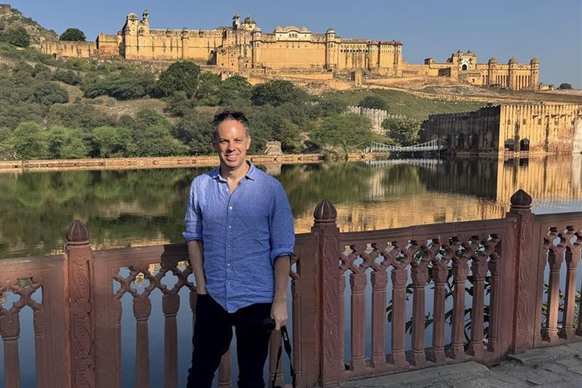 Person in front of Amer Fort with a lake reflection, under a clear blue sky.