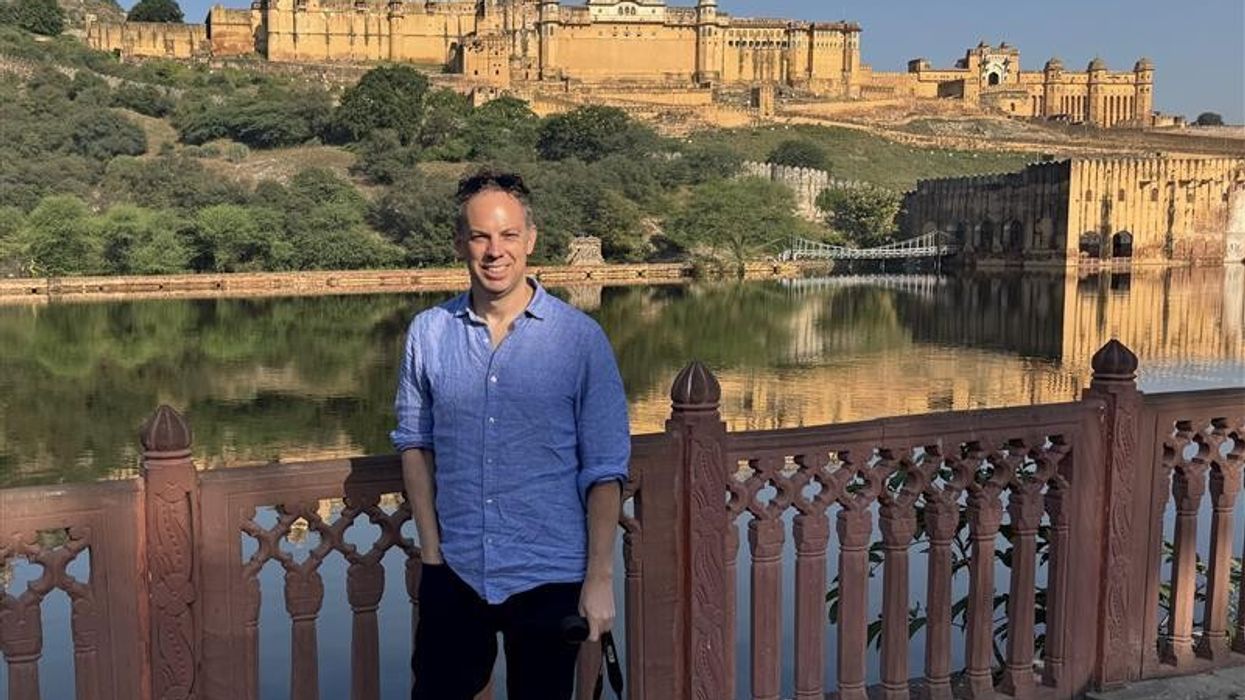 Person in front of Amer Fort with a lake reflection, under a clear blue sky.