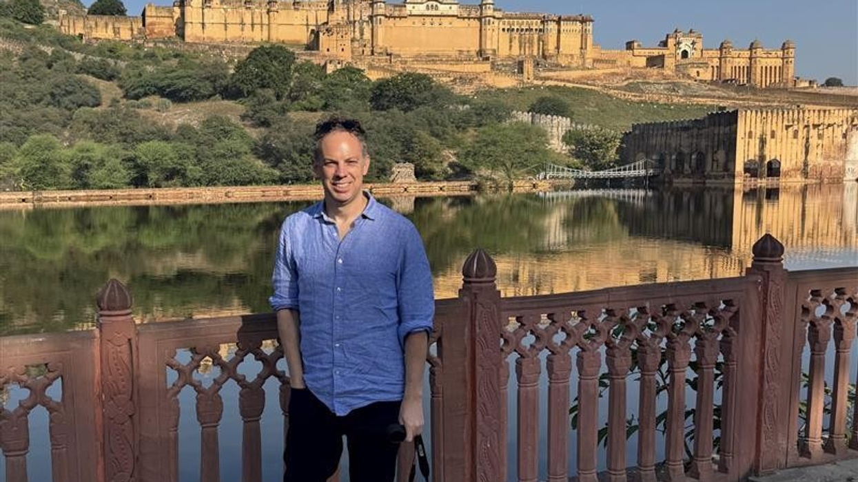 Person in front of Amer Fort with a lake reflection, under a clear blue sky.