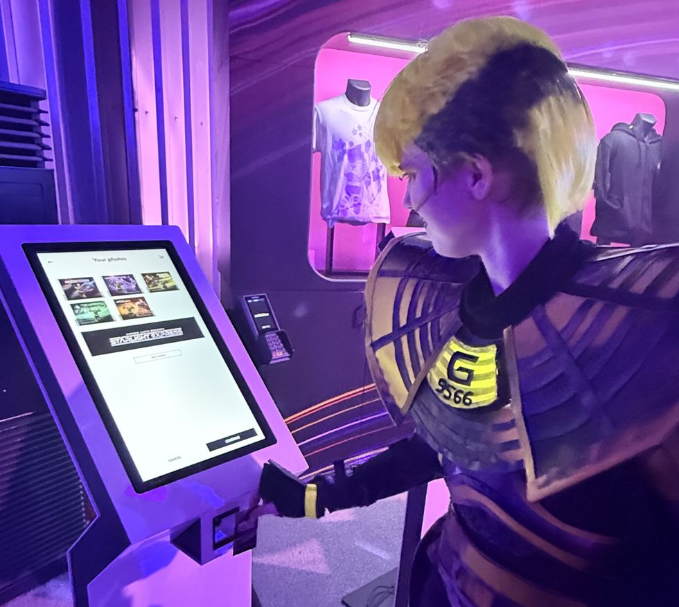 Person in futuristic costume using GoPhoto touchscreen kiosk under purple lighting during Starlight Express at Wembley