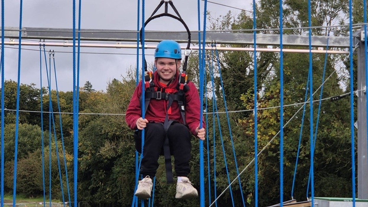 Person in helmet and harness on a high ropes course, smiling at the camera.