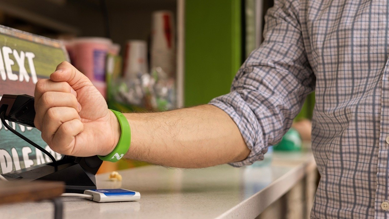 Person in plaid shirt paying with wristband at a card reader.