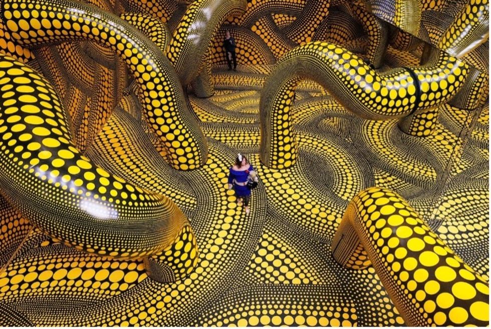 Person in polka-dotted, yellow and black art installation with large curving structures.