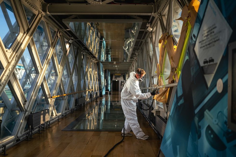 Person in protective gear coating windows inside a bridge's glass walkway.