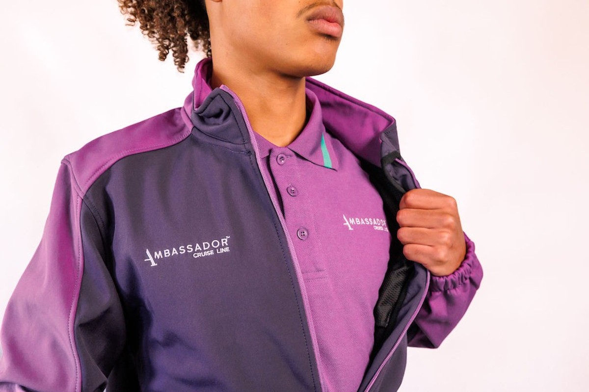 Person in purple Ambassador Cruise Line uniform, jacket partially open, white background.