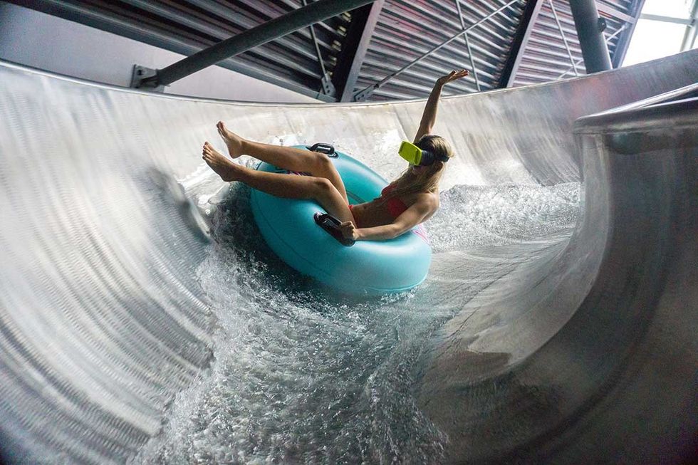 Person in red swimsuit and VR headset on water slide with blue inner tube at Therme Erding
