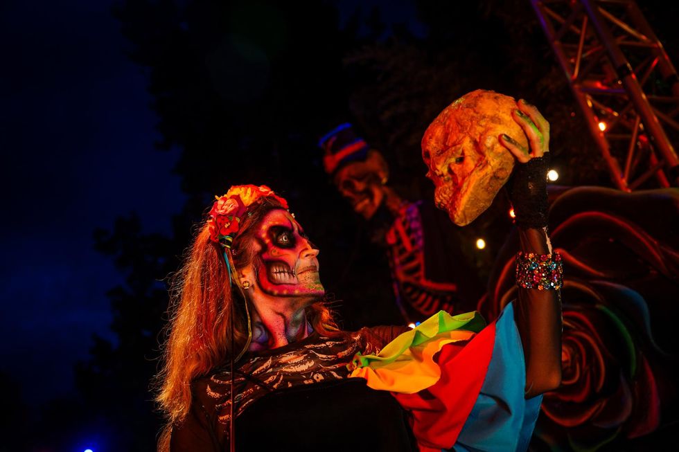 Person in skull makeup holds a skull, with vibrant attire and dark background lighting at Six Flags Great Adventure