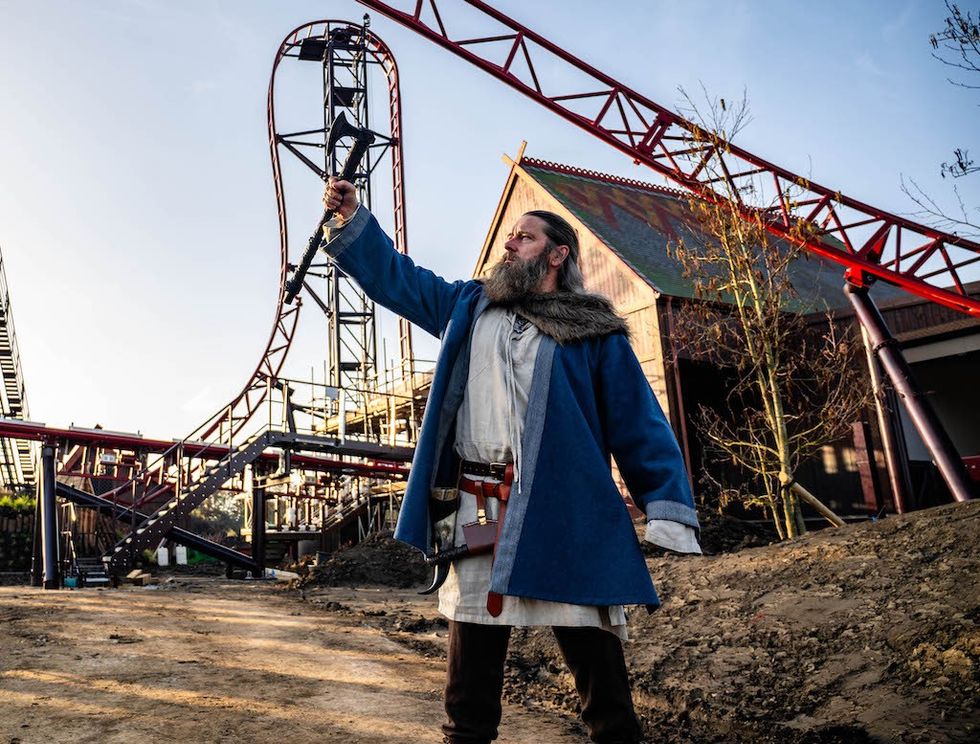 Person in Viking attire holding an axe in front of a red roller coaster track.