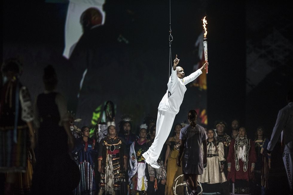 Person in white holding torch, suspended above a crowd in traditional attire.