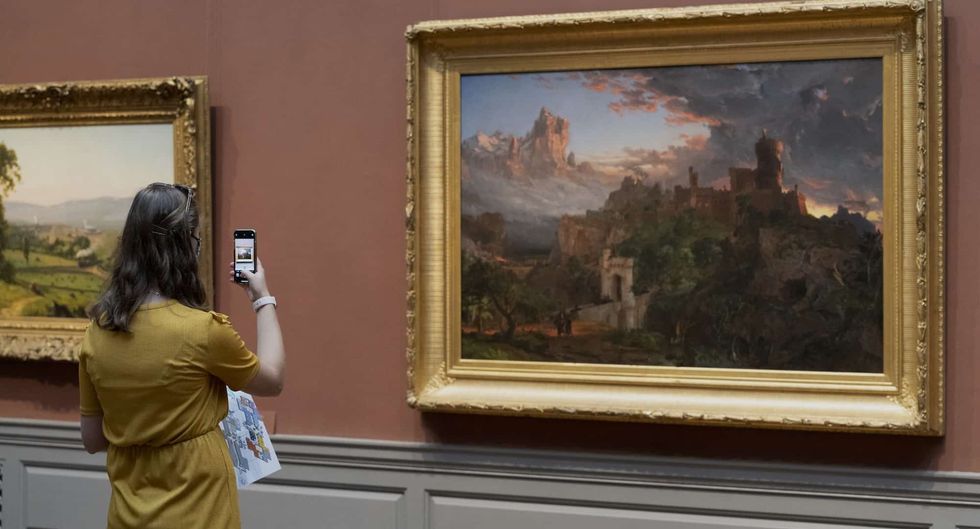 Person in yellow photographing a framed painting in a gallery at National Gallery of Art