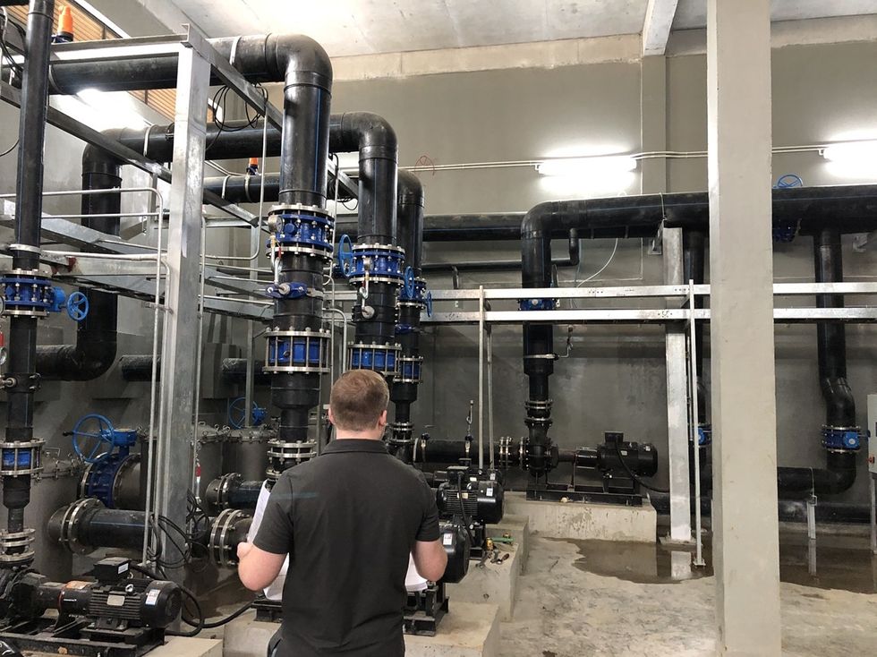 Person inspecting an ozone system with black pipes and blue valves.