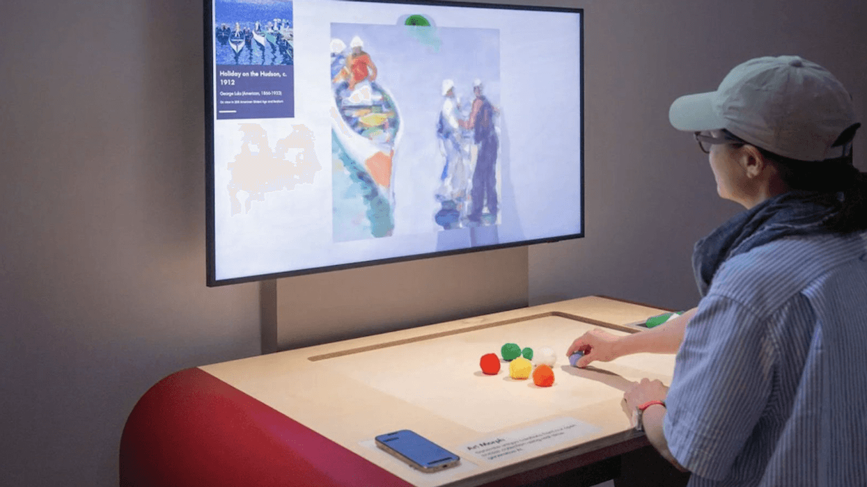 Person interacting with an art display using colored blocks on a tabletop screen.