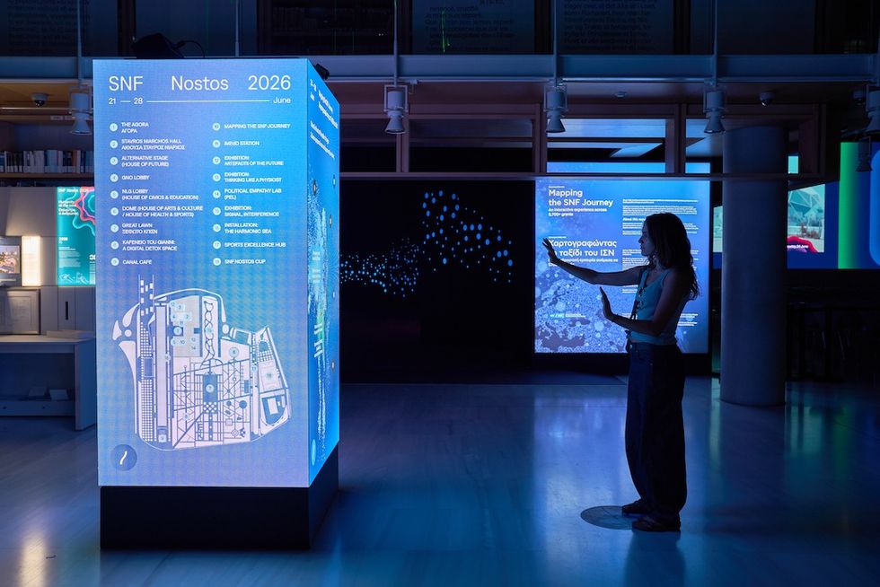 Person interacting with illuminated digital display in a dimly lit exhibition space.