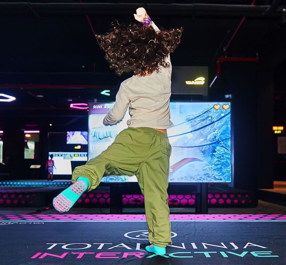 Person jumping energetically on an interactive floor, facing a large screen game display.