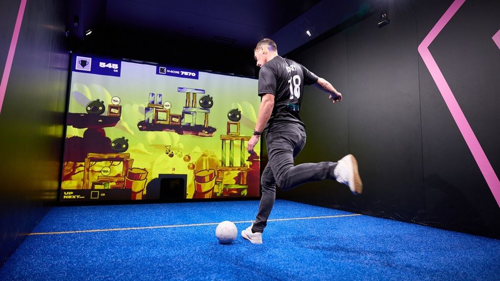 Person kicks soccer ball towards interactive gaming screen.