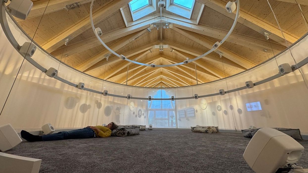 Person lying on carpeted floor in large, modern room with skylights and circular seating at Klanghaus and Peter Roth Resonance Centre