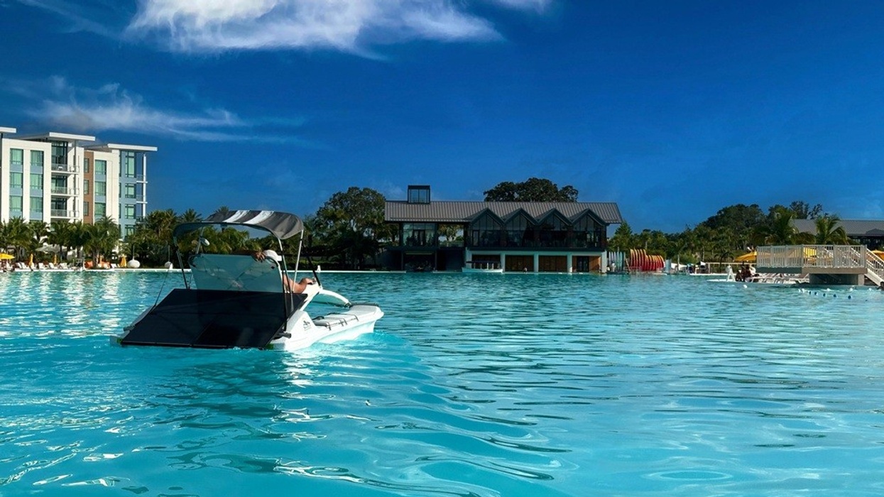 Person on a boat in a large pool, with buildings and trees in the background.