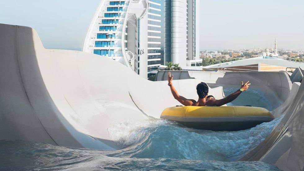 Person on a waterslide raft with cityscape and ferris wheel in the background at Wild Wadi Waterpark