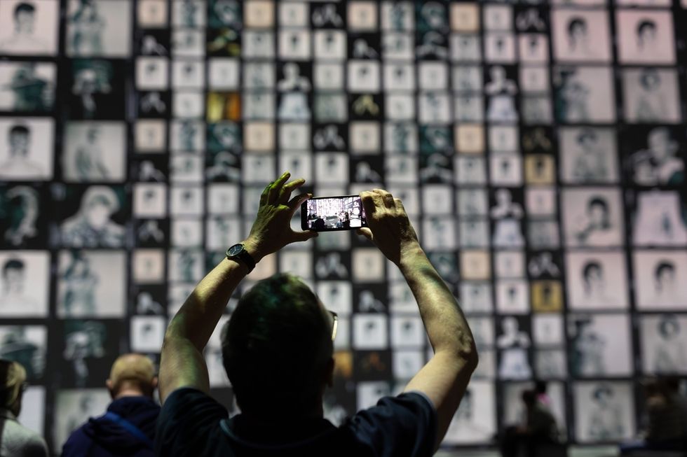 Person photographing a wall of black-and-white portraits with a smartphone.