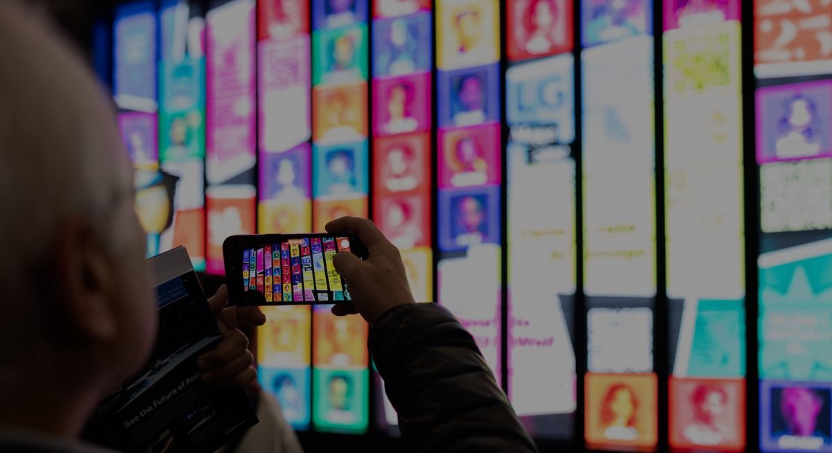 Person photographing a wall of colorful, digital screens with a smartphone.
