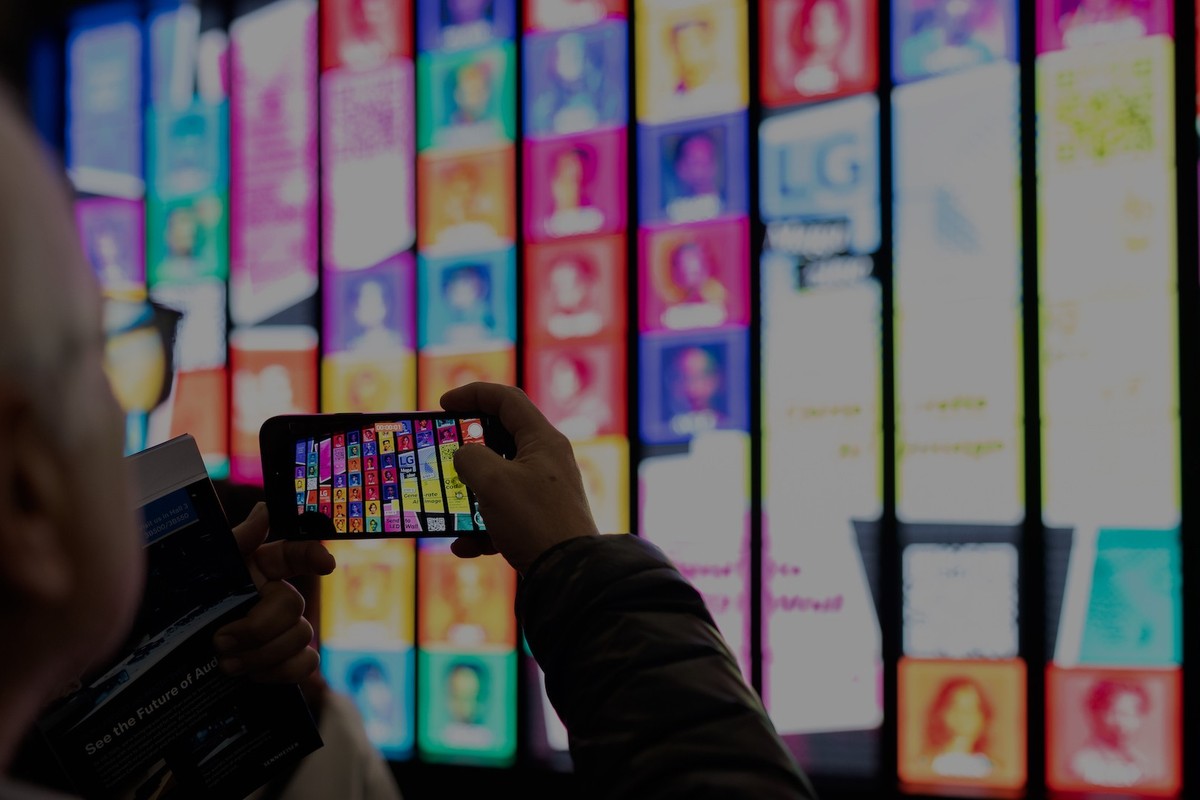 Person photographing a wall of colorful, digital screens with a smartphone.