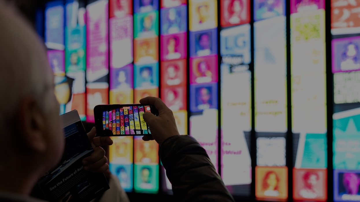 Person photographing a wall of colorful, digital screens with a smartphone.