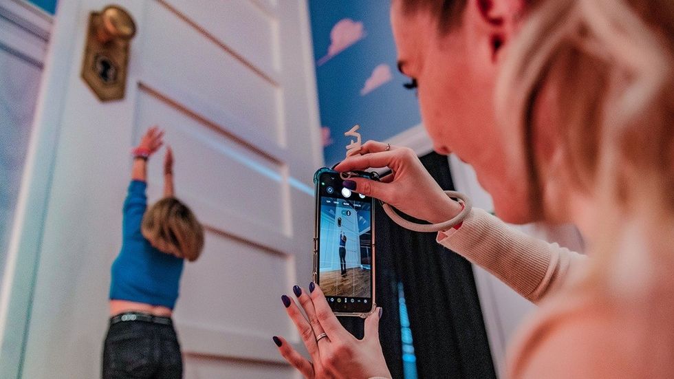 Person photographing another reaching for oversized door, creating an illusion of smallness.