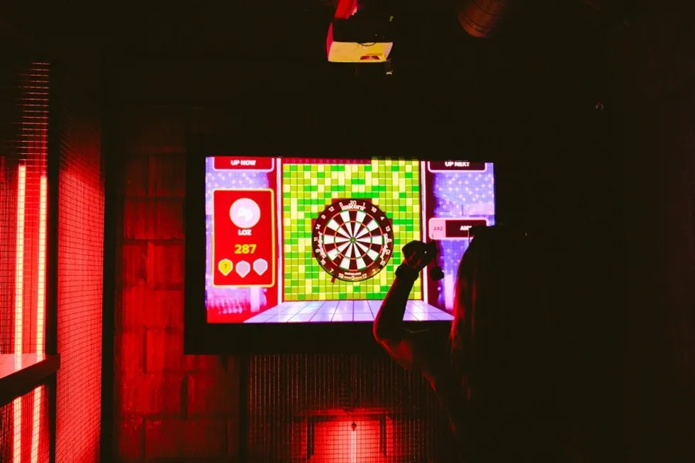 Person playing digital darts game in a dimly lit room with red lighting.