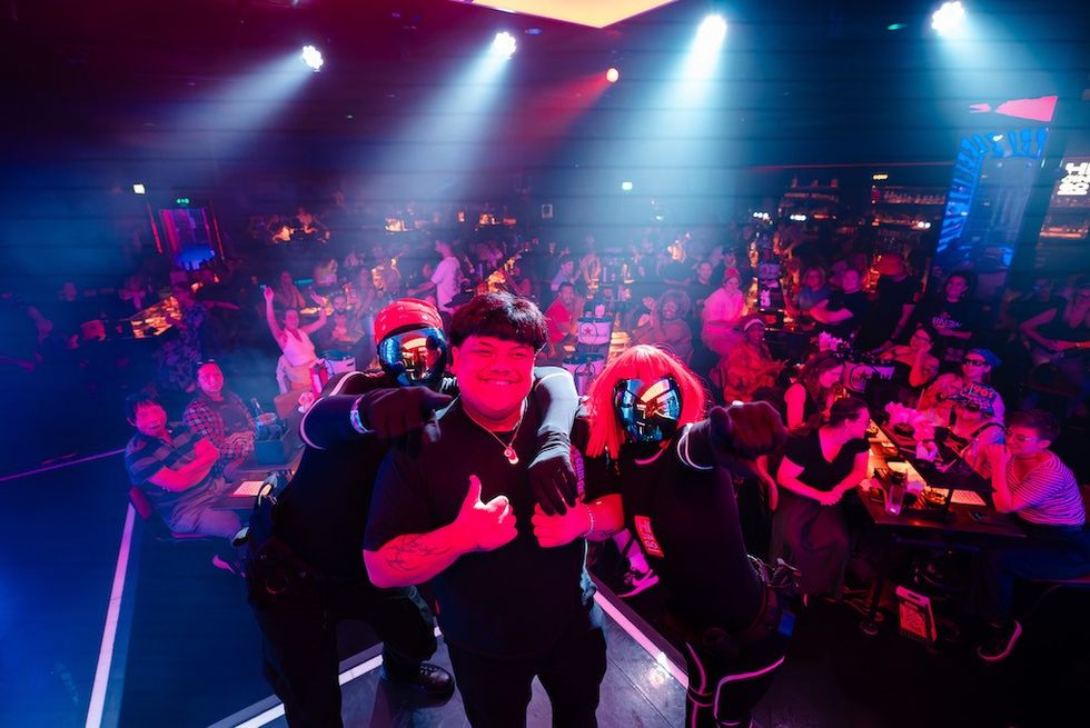 Person posing with two costumed characters on stage, audience cheering in the background.