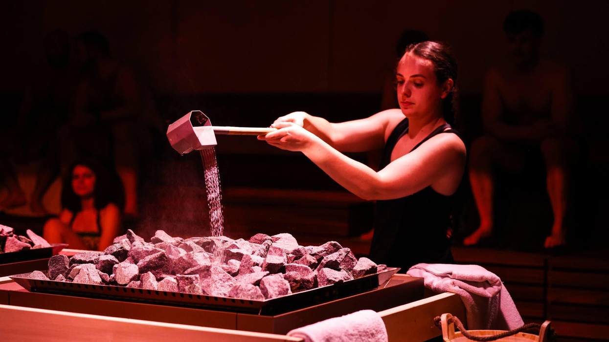 Person pouring water over hot stones in a sauna, creating steam.
