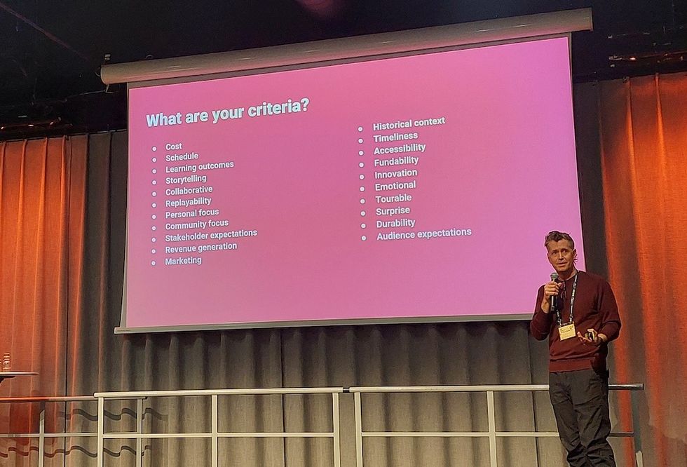 Person presenting criteria list on a pink screen at a conference.
